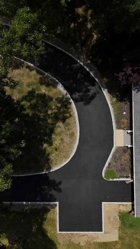 Aerial view of a new asphalt driveway curving through a lawn to a turnaround