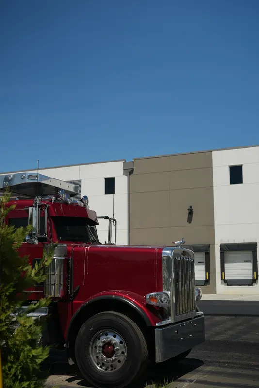 Red dump truck parked on new asphalt beside a warehouse