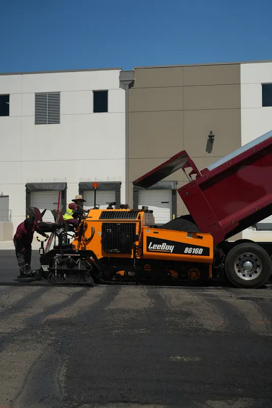 Dump truck loading hot asphalt into the paving machine at a commercial lot