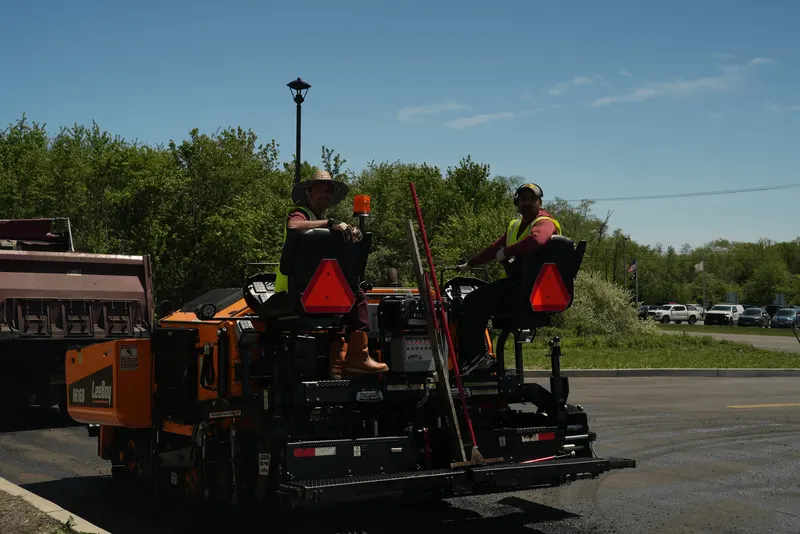 Crew members riding the paving machine on a commercial parking lot