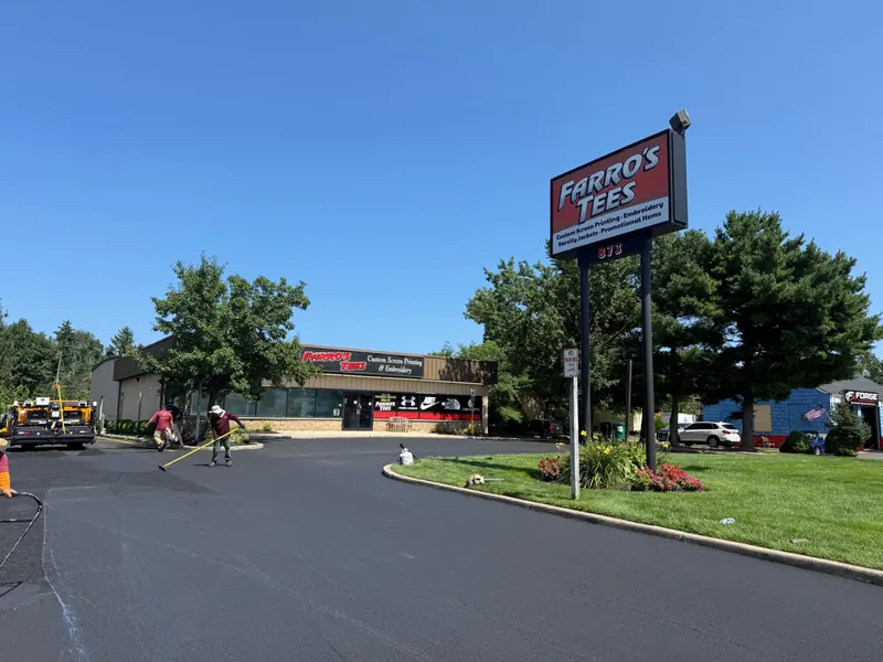 Dan The Paver crew raking fresh asphalt while paving a commercial parking lot in Monmouth County, with the paving machine behind them