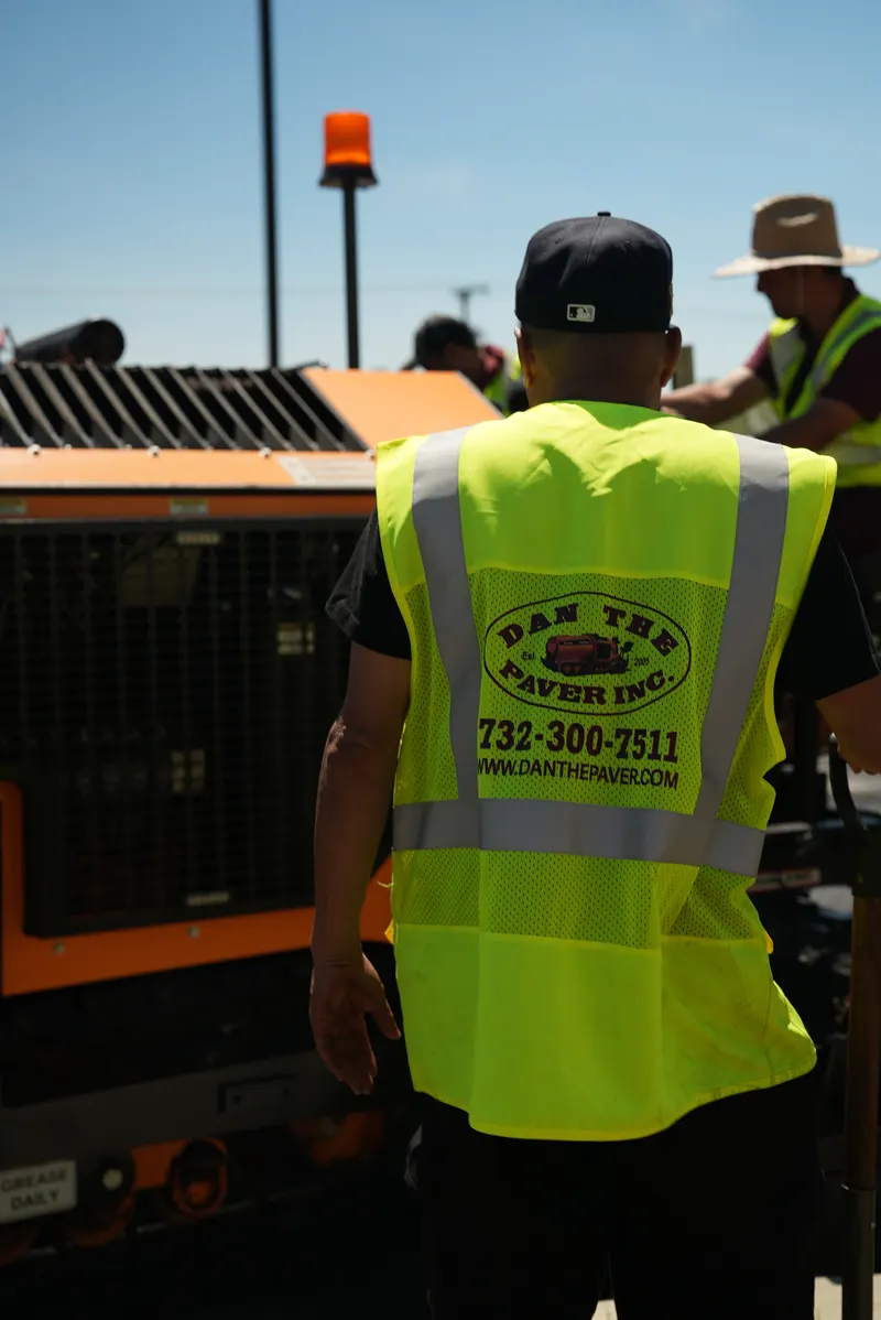 Crew member in a Dan The Paver safety vest standing beside the paving machine on a job