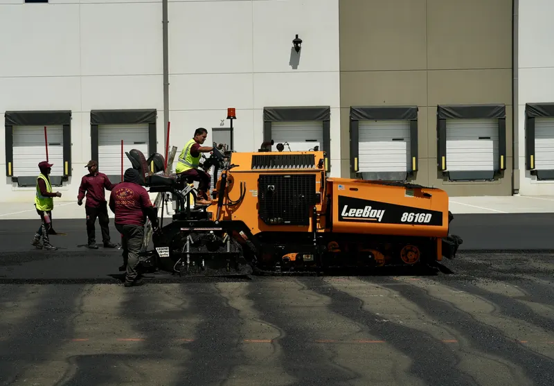 Crew guiding the paving machine in front of warehouse loading docks