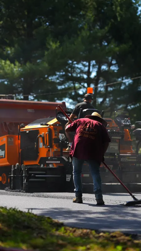 Crew member raking hot asphalt beside the paving machine on a residential driveway