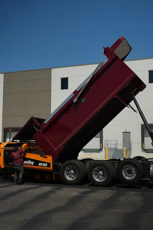 Dump truck bed raised to tip asphalt into the paving machine hopper