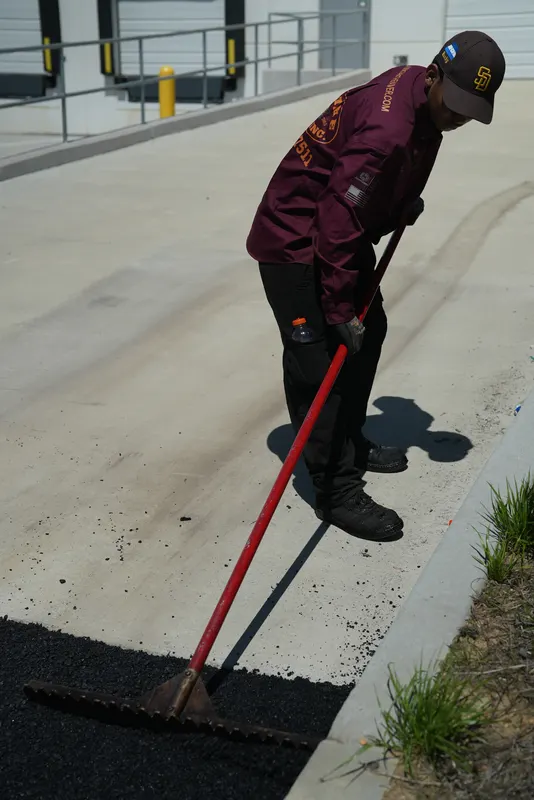 Crew member using a lute to shape the asphalt edge against a curb