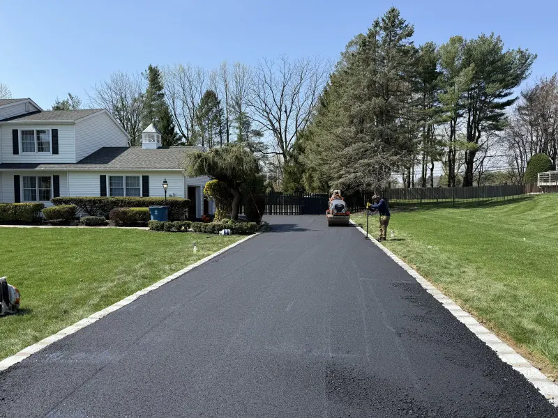 Freshly paved asphalt driveway with block edging leading up to a white colonial home