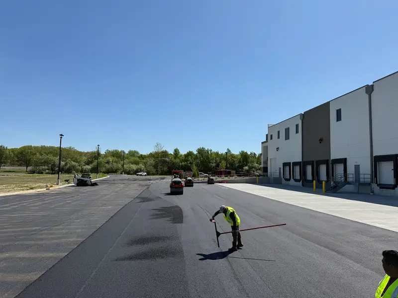 Crew checking fresh asphalt while rollers compact a new parking lot in New Jersey