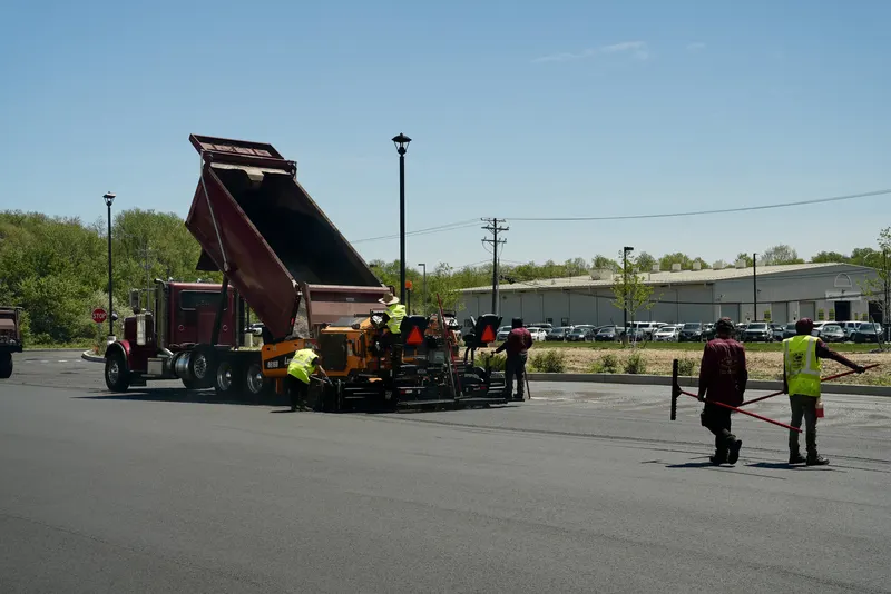 Dump truck feeding the paving machine as the crew paves a large parking lot
