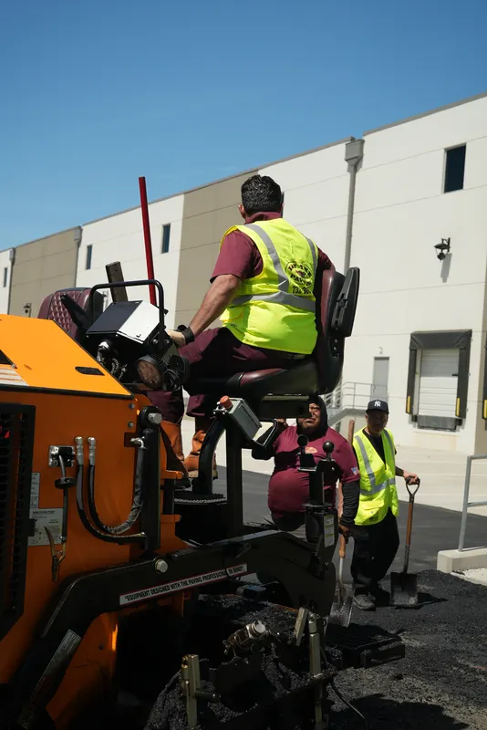 Operator driving the paving machine as the crew lays a parking lot