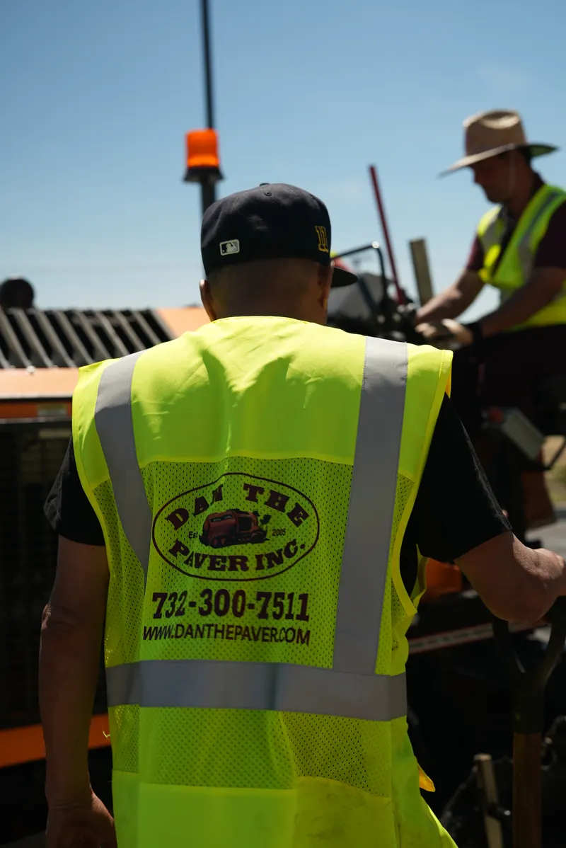 Crew member in a Dan The Paver safety vest stepping up to the paving machine