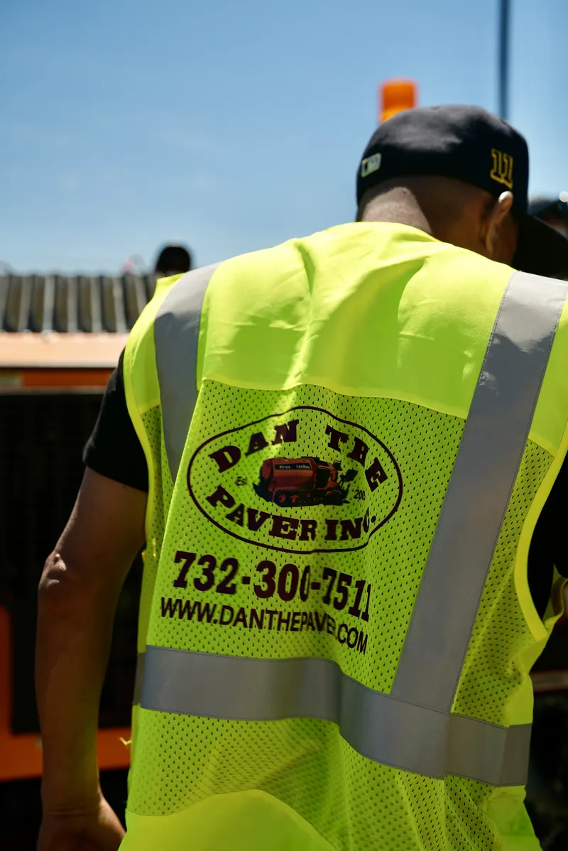Dan The Paver crew member in a branded safety vest walking past the paving machine