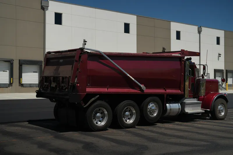 Tri-axle dump truck delivering hot asphalt to a warehouse parking lot
