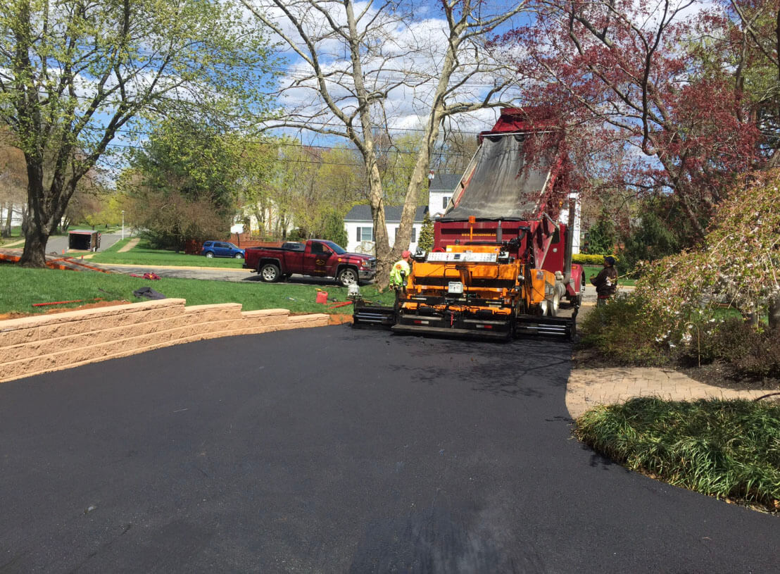 Dan the Paver team applying hot asphalt to residential driveway with paving machine.