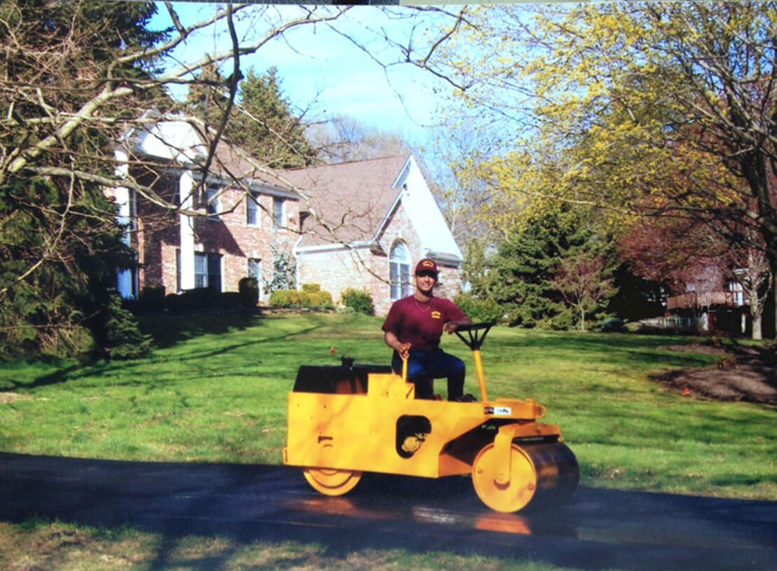 Dan the Paver team member using a paving roller to smooth a newly paved asphalt surface.