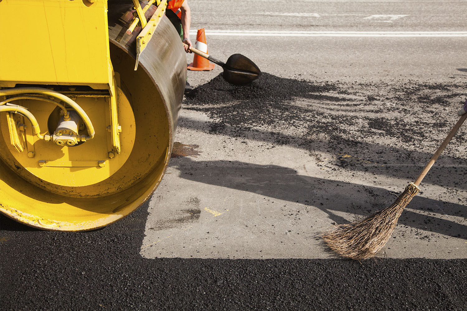A worker laying fresh asphalt bitumen on a driveway, with shovels and other tools nearby.
